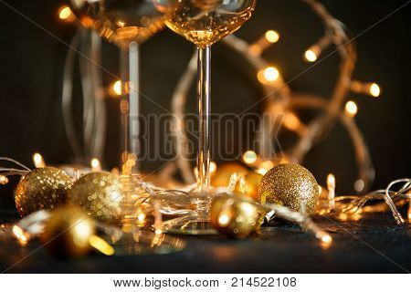 Two glasses for wine and golden Christmas balls against a background of blurred golden lights. Shallow depth of field.