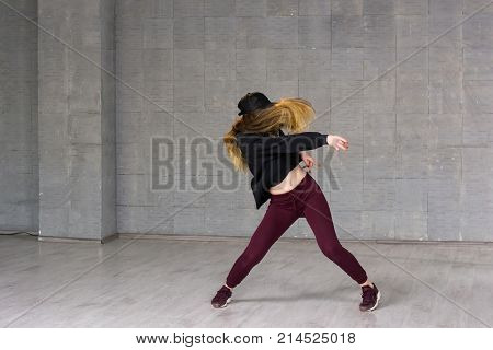 Female hip-hop dancer in motion. Young caucasian woman dancing modern dance on grey background. Street dance performance.