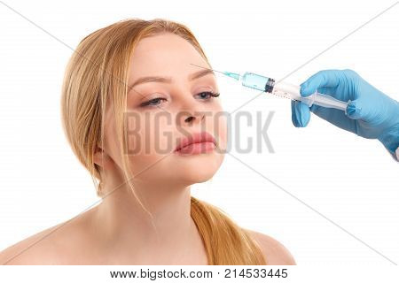 The doctor in a white dressing gown and medical gloves makes an injection in the forehead area of a beautiful blond woman. Isolated on white background.