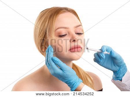 The doctor makes an injection to increase the lips of a young girl with blond hair. Isolated on white background.
