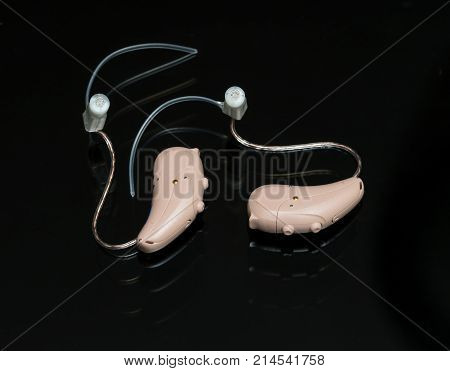 Macro close up of a matched pair of tiny modern hearing aid on black reflective background