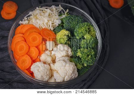 Fresh organic broccoli cauliflower cabbage and carrots on dark background. Vegetarian food table ingredients. Healthy food concept.