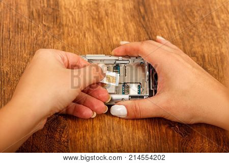 change of the SIM card in a smartphone on wooden table. female hands insert a SIM card in the phone