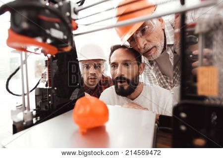 Three men are working to prepare printed model on the 3d model of the heart. They are satisfied with the result. They peer through the working field 3e of the printer.
