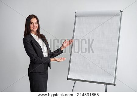 Portrait of young smiling businesswoman standing by flipchart in office.