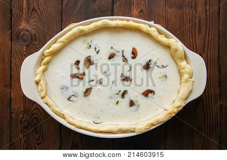 Half-finished Quiche With Mushrooms And Cheese Ready To Bake In A Ceramic Dish On A Wooden Backgroun