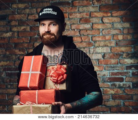 The positive Redbeard male holds Christmas gifts over the wall of a brick.