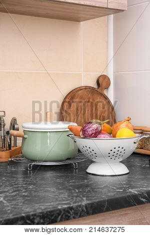 Colander with vegetables and stewpan on table in kitchen