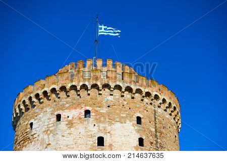 The White Tower in Thessalonica and waving Greek flag, Greece                               