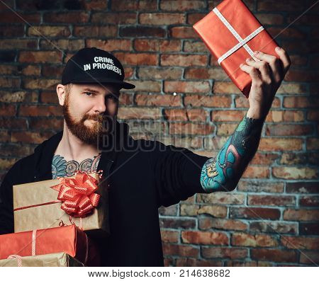 The positive Redbeard male holds Christmas gifts over the wall of a brick.