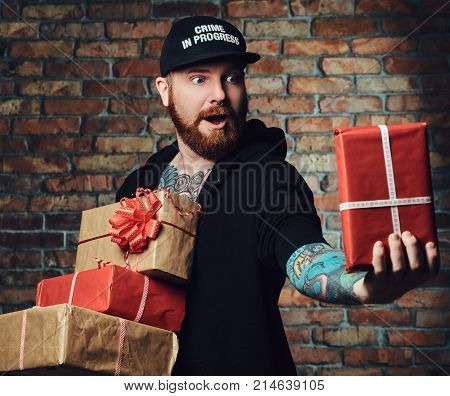 The positive Redbeard male holds Christmas gifts over the wall of a brick.