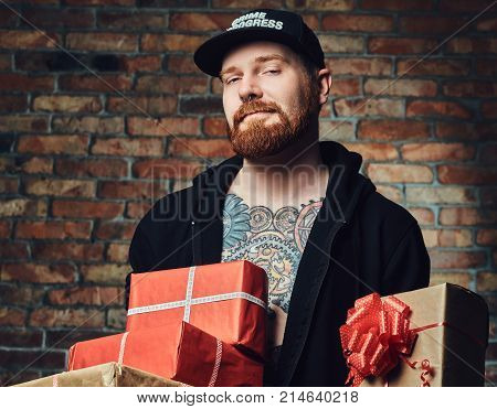 The positive Redbeard male holds Christmas gifts over the wall of a brick.