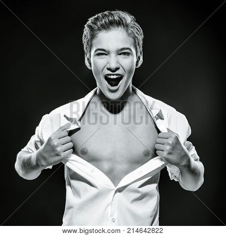 Photo of guy at the age of a teenager tearing shirt on chest. Teen boy screeming. Black and white image