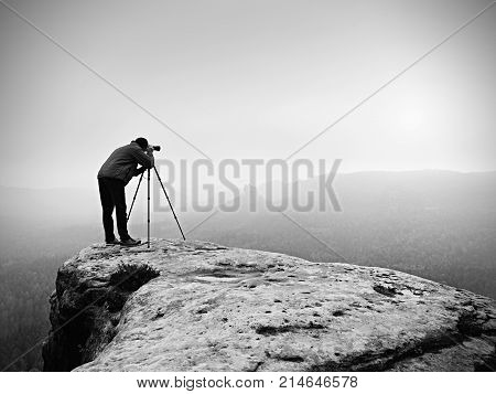 Hiker With Camera On Tripod Takes Picture From Rocky Summit. Alone Photographer  On Summit