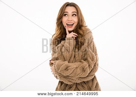 Image of young cheerful woman dressed in warm sweater standing isolated over white wall background. Looking aside.