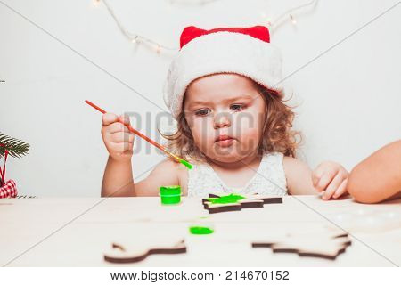 Adorable girl is painting wooden Christmas figurines