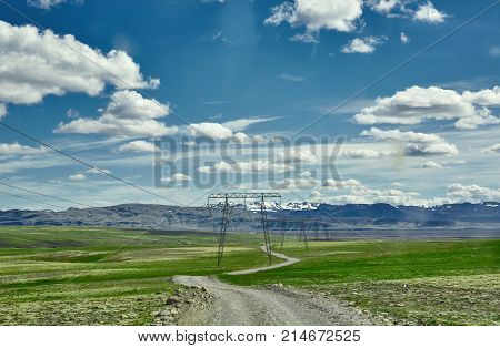 Travel to Iceland. road and high voltage power transmission line in a bright sunny mountain landscape. Vatna volcano covered with snow and ice on tne background.