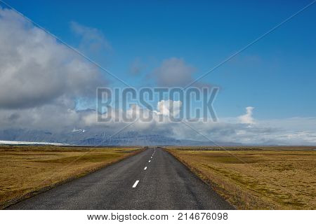 Travel to Iceland. road in a bright sunny mountain landscape. Vatna volcano covered with snow and ice on tne background.