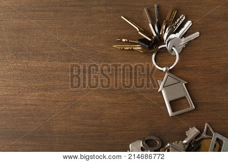 Bunch of keys with house shaped trinklet against wooden background and collection of different keys. Safety, security and real estate concept, top view, copy space