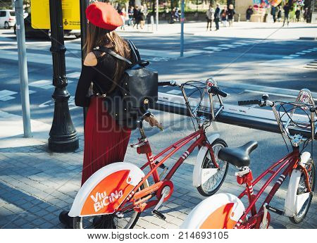 BARCELONA SPAIN - NOV 12 2017: Stylish Spanish woman wearing red beret hat resting near the free public bicycles Viu Bicing