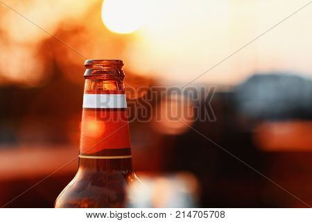 Beer Bottle Against Summer Sky At Sunset On Blurry Background With Lens Flare