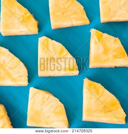 Close up patter of many pieces of yellow pineapple laying on blue wooden table background.