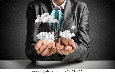 Closeup of business woman in suit presenting flying aerostate among clouds in her palms with dark wall on background. 3D rendering.