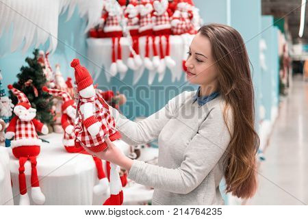 Cheerful happy customer girl choosing gifts for Christmas and New Year. She is holding snowman toys