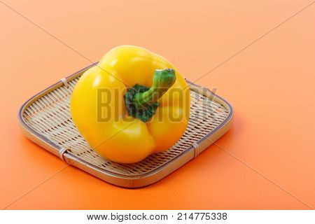 Beautiful of sweet yellow bell pepper isolated in bamboo basket on orange background.