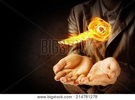Closeup of businessman in black suit keeping flaming key symbol in hands with dark wall on background.