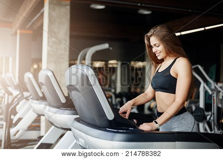 Young beautiful woman programming a threadmill to make her morning jog even harder. Female coach warming up before a long day at work.