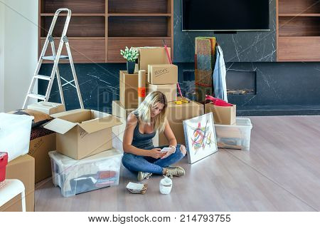 Woman unpacking moving boxes and looking cell phone