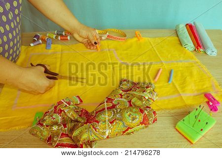 Close up of woman's hands drawing a pattern on yellow tissue. Measuring tape and sewing accessories. A tailor is laying out a dress/Sewing layout