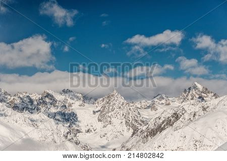 Scenic view of winter mountains covered with snow under the clouds in the clear blue sky