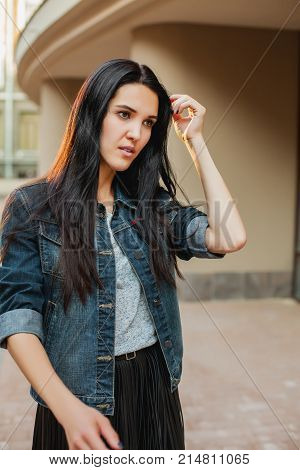 thoughtfull young woman in a gray shirt black leather skirt and jeans jacket walking around city. Concept of modern freedom hipster human