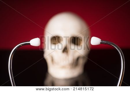 Stethoscope i focus and blurry skull isolated on black red background