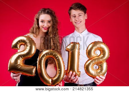 Young couple friends female woman and male man holding gold balloons numbers 2018 as symbol of New Year on red background