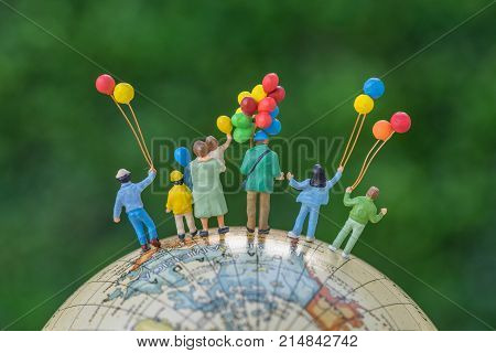 miniature people figure back view of happy family holding balloons standing on globe as world climate change environment or happy family concept.