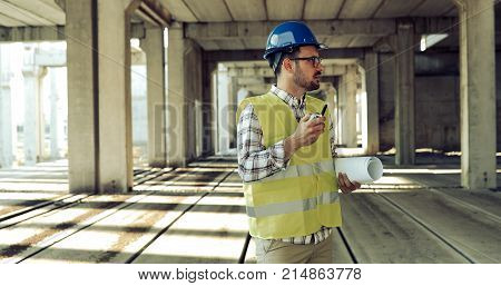 Male architect with blueprints using walkie-talkie at construction site