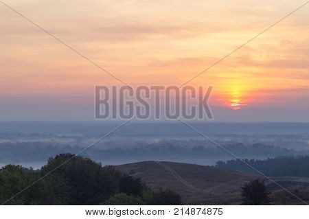 Morning autumn landscape: fog over hills and forest on background of red sunrise. View from above. Village Opishnya Poltava region Ukraine