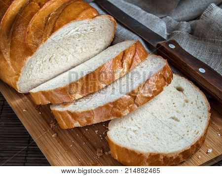 Fresh delicious aromatic appetizing white bread made of wheat flour for breakfast lunch dinner ready to eat cut into pieces on a wooden kitchen board on a table next to a napkin on which lies a knife with a wooden handle
