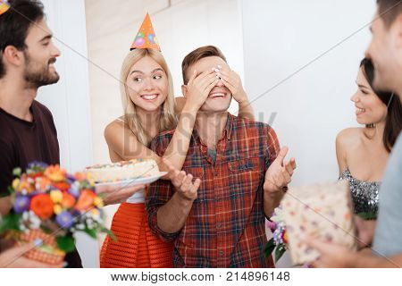 The girl has prepared the guy a surprise for birthday. She closed his eyes by hands. She smiles and leads the guy to a surprise. Guests are standing around them.