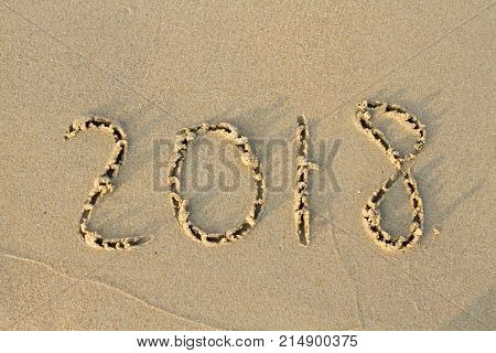 New Year 2018 is coming concept. wave coming to 2018 concept on the sand beach in the morning.Text 2018 on a beach sand. Concept New Year 2018 is coming soon