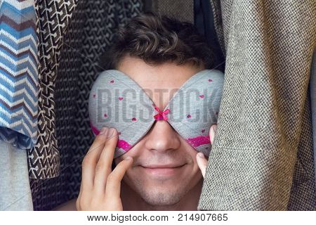A young man in the closet with a bra on his face.