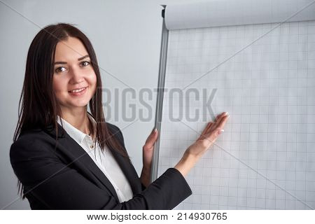 Attractive smiling young woman writing on a blank flipchart in an office as she does a presentation or promotion