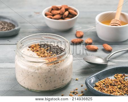 Overnight oats in jar and ingredients - chia seeds, almond, honey and pollen on gray wooden table background. Healthy breakfast oatmeal recipe idea