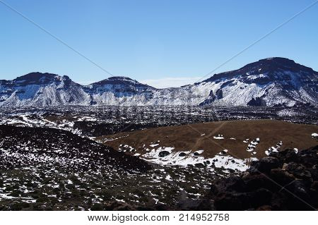 White snow on brown and black lava fields in the volkano Teide.