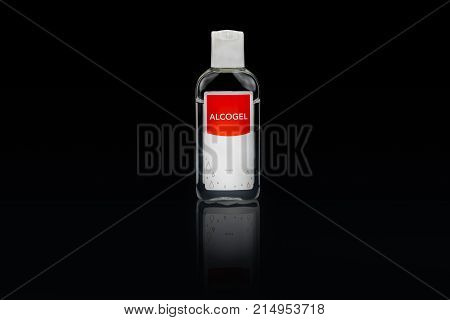 Isolated alcogel hand disinfectant in a small plastic bottle with red label studio shot on black background.