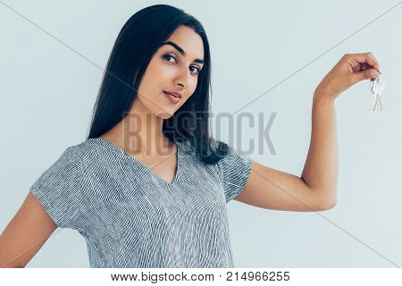 Closeup portrait of young confident pretty Indian woman looking at camera and holding keys. Isolated view on white background.
