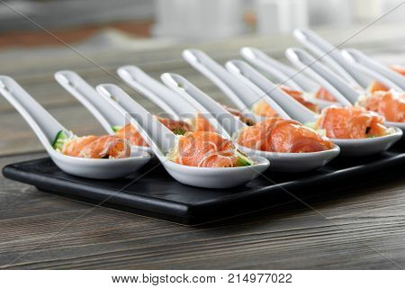 Smoked salmon rolls with cheese filling served in big portion spoons on black plate on wooden table copyspace layout background delicious tasty appetizers restaurant concept.
